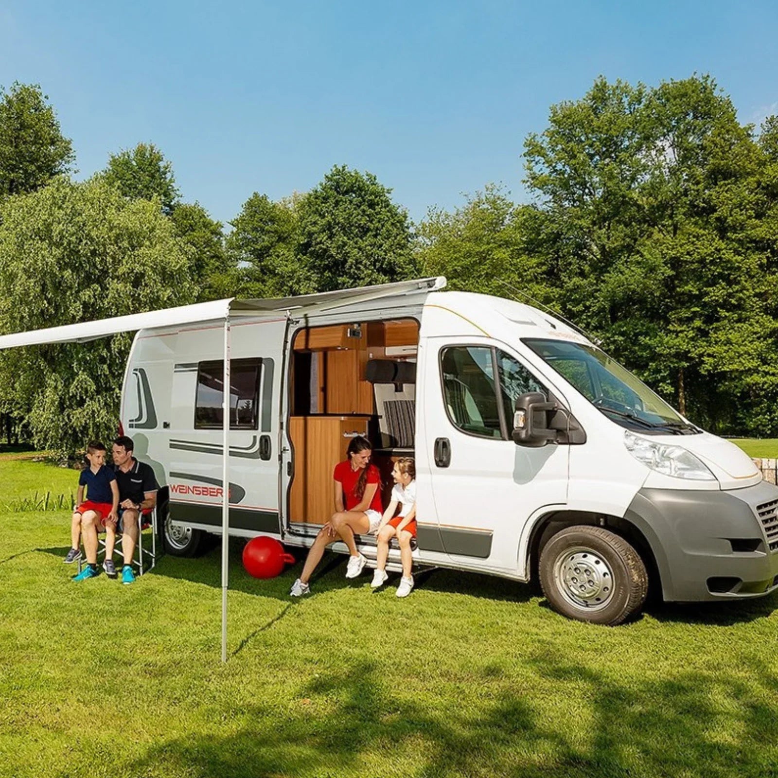 Family relaxing beside campervan with awning on grassy site, ideal for off-grid adventures